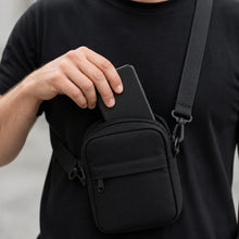 Mão guardando um celular dentro da shoulder bag preta, mostrando que o celular cabe